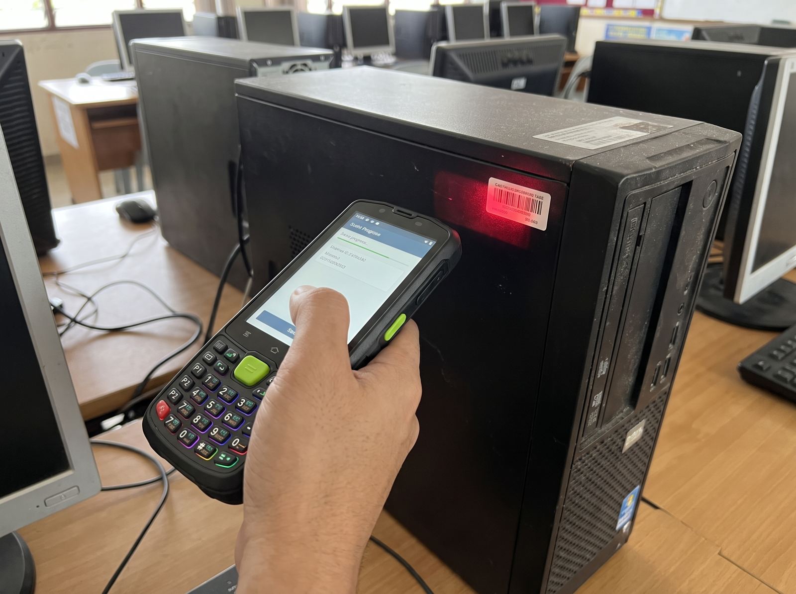Handheld scanner reading a barcode asset tag on a school computer