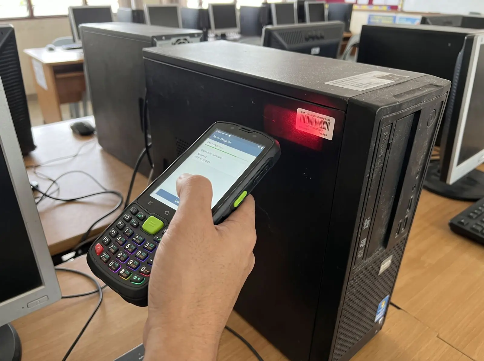 Handheld scanner reading a barcode asset tag on a school computer